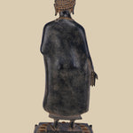 Back view of a standing brass sculpture of Lord Buddha, showing the details of his robe's drape, the intricate design of his hair, and the lotus pedestal