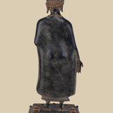 Back view of a standing brass sculpture of Lord Buddha, showing the details of his robe's drape, the intricate design of his hair, and the lotus pedestal