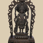 Four-armed dark brass idol of Lord Vishnu standing on a lotus pedestal within a decorative arch. He holds the conch (shankha), discus (chakra), a lotus (padma), and a mace (gada), symbolizing his divine power and preservation.