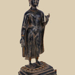 Brass sculpture of Lord Buddha standing with one hand raised in the Vitarka mudra (gesture of teaching and discussion), wearing flowing robes and standing on a detailed lotus pedestal.