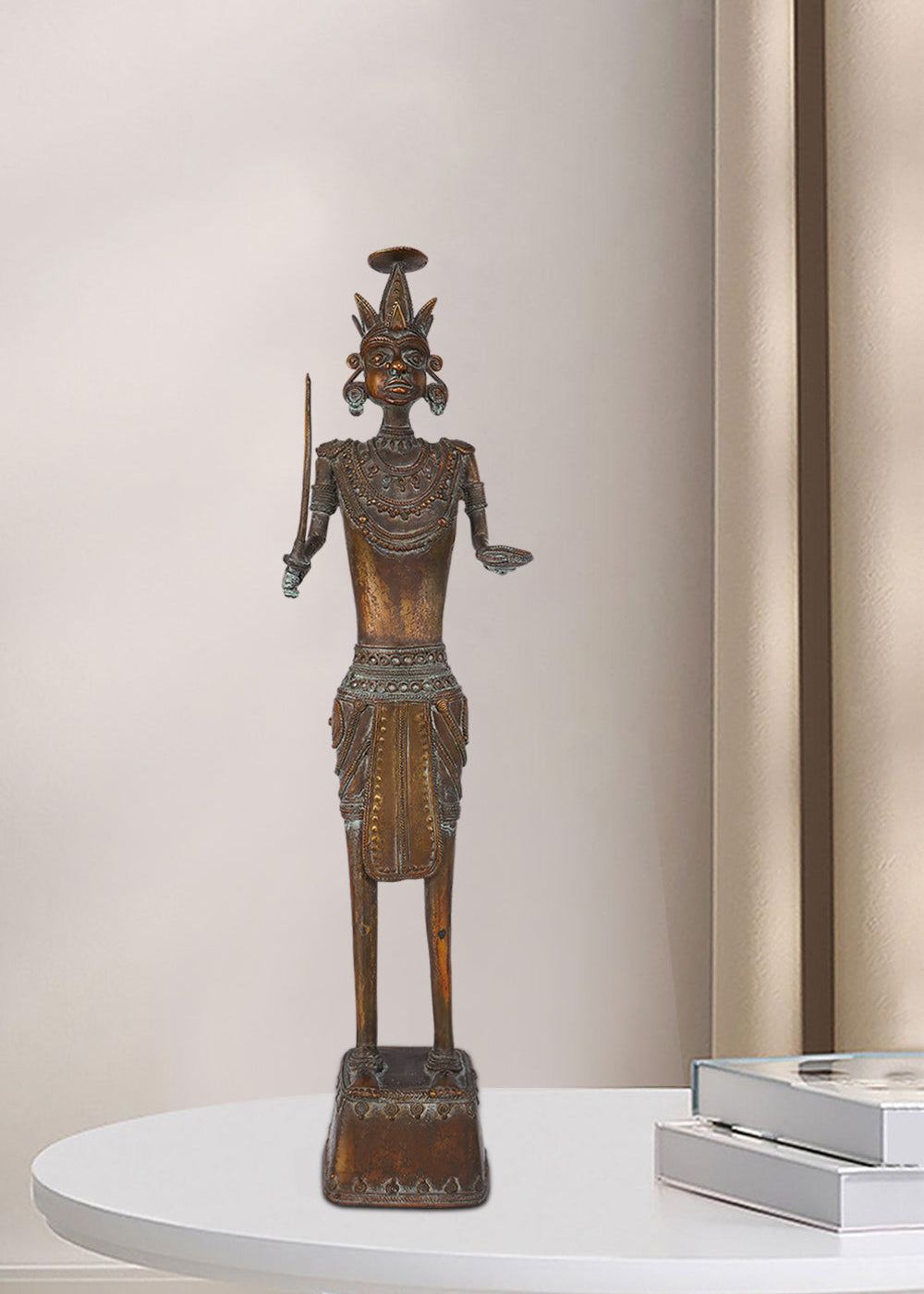 Dark brass figure of a tribal warrior holding a sword in one hand and an open palm in the other, featuring intricate jewelry, a unique headdress, and standing on a decorated pedestal.