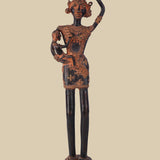 Antique dark brass sculpture of a tribal woman carrying a child in her arms and a pot on her head, adorned with traditional jewelry and standing on a decorated pedestal. The artwork reflects rural life and motherhood.
